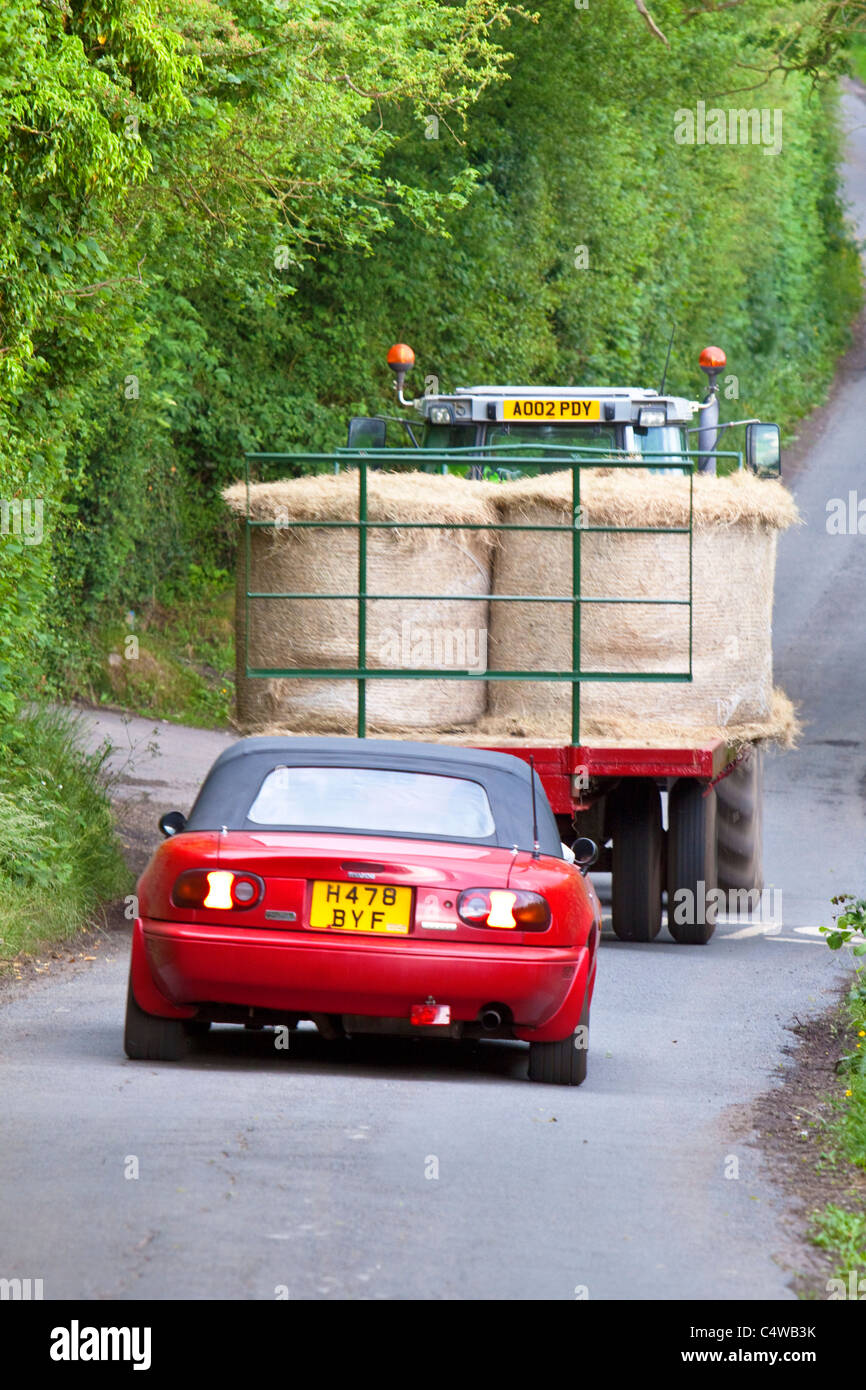 Roter Sportwagen hinter Traktor auf Land Lane, England, UK Stockfoto