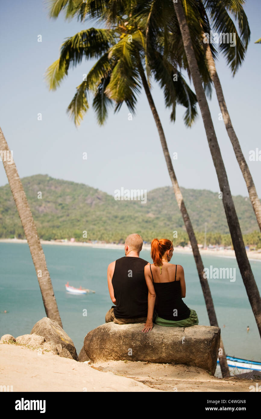 Ein paar junge Touristen sitzen hoch unter den Palmen hoch über dem Meer in Palolem Beach in Zustand von Goa, Indien Stockfoto