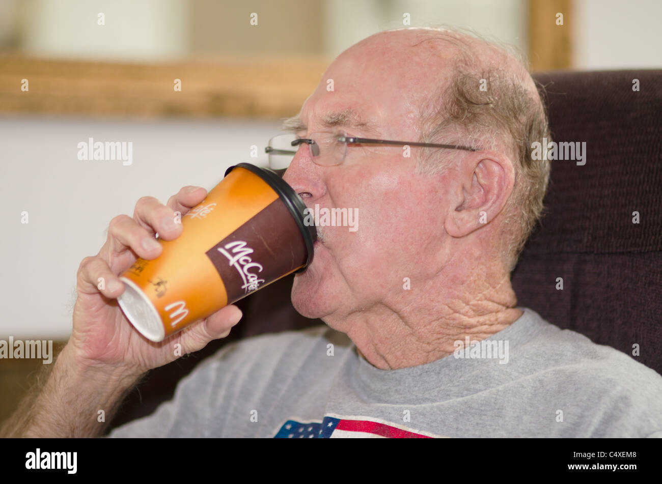 Ein älterer Mann Causasian Getränke Kaffee aus einem McDonald's Cup in seinem eigenen Haus. USA Stockfoto