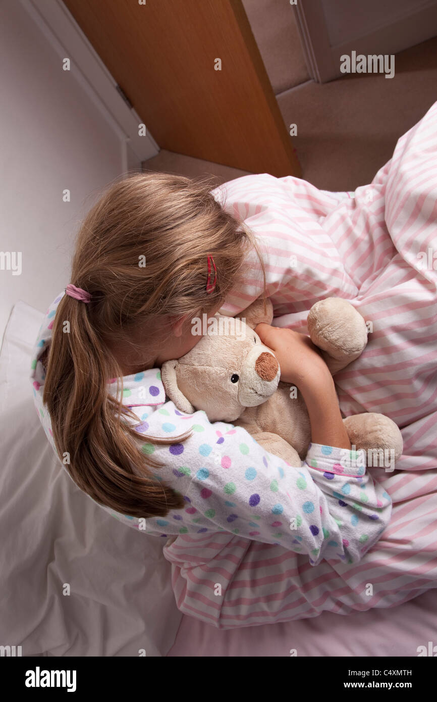 Junges Mädchen kuscheln einen Teddybär sitzt auf dem Bett, Kopf nach unten. Stockfoto