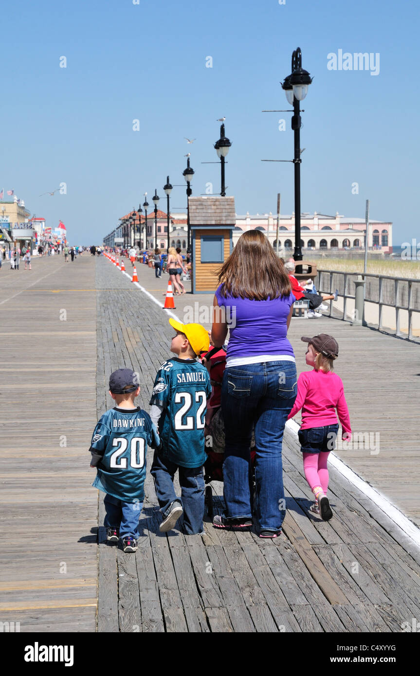 Eine Frau mit drei kleinen Kindern zu Fuß neben ihr. schiebt einen Kinderwagen auf der Promenade in Ocean City, New Jersey Stockfoto