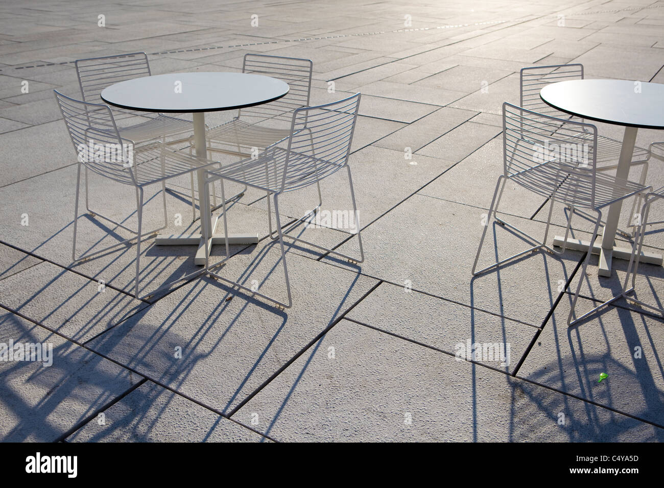 Runden Tisch/s und Stühle auf einem gefliesten Boden Schatten offenbart sich durch eine absteigende Sonnenuntergang Stockfoto