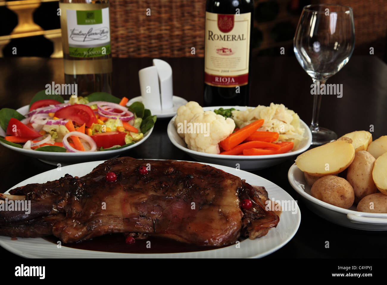 Lammkeule mit Johannisbeer-Sauce und gekochten Kartoffeln Gemüse Salat und Flaschen Wein Stockfoto