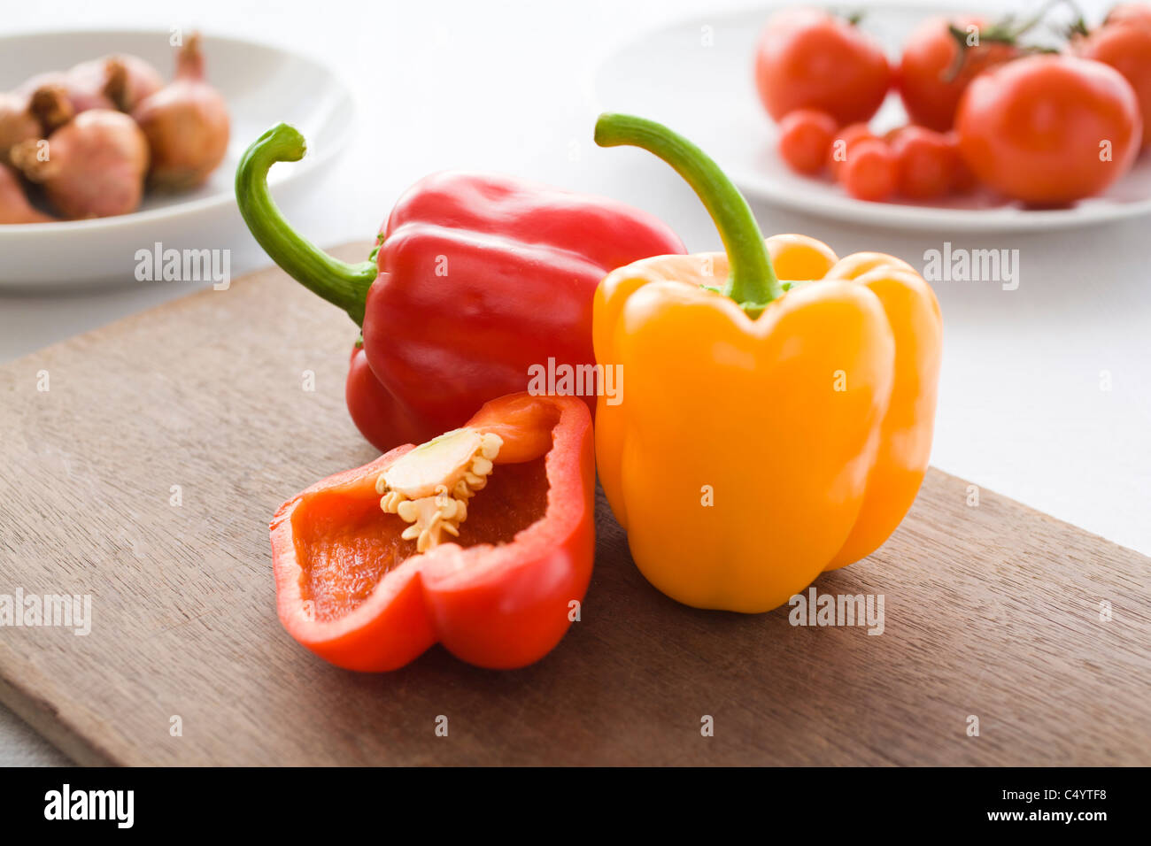 Rote und gelbe Paprika, geschnitten und ganze, auf ein Schneidbrett aus Holz begleitet von anderen Gemüse in eine Tischdekoration Stockfoto