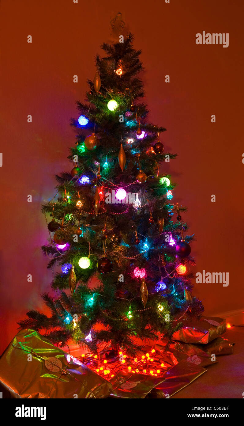 Weihnachtsbaum mit Lichtern und Geschenke rund um die Basis. Stockfoto