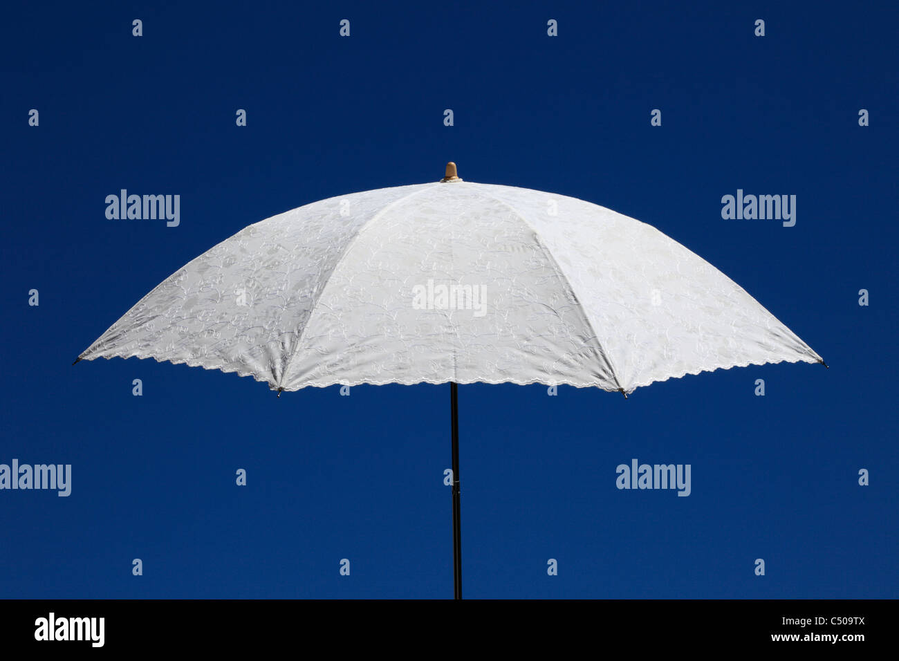 Ein Hand gehaltenen weißen Leinen Sonnenschirm mit gestickten Details, legen Sie gegen einen klaren, blauen Sommerhimmel. (Hochformat Ref C509TF) Stockfoto