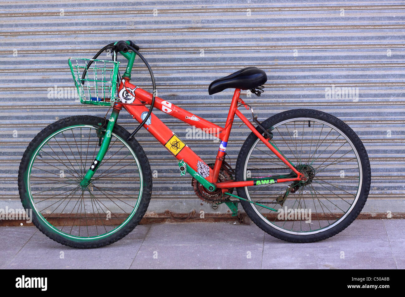 Eine personalisierte roten und grünen Fahrrad gelehnt eine Fensterläden Ladenfront mit Korb, Fahrradschloss, hängen über den Lenker. Stockfoto