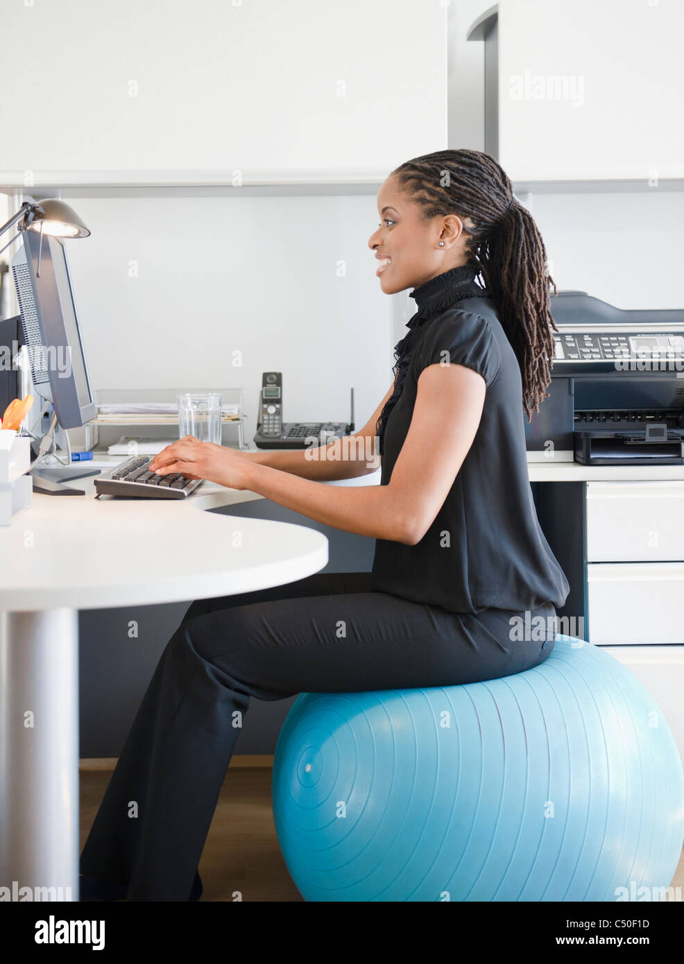 Afrikanische amerikanische Frau auf Gymnastikball am Schreibtisch sitzend Stockfoto