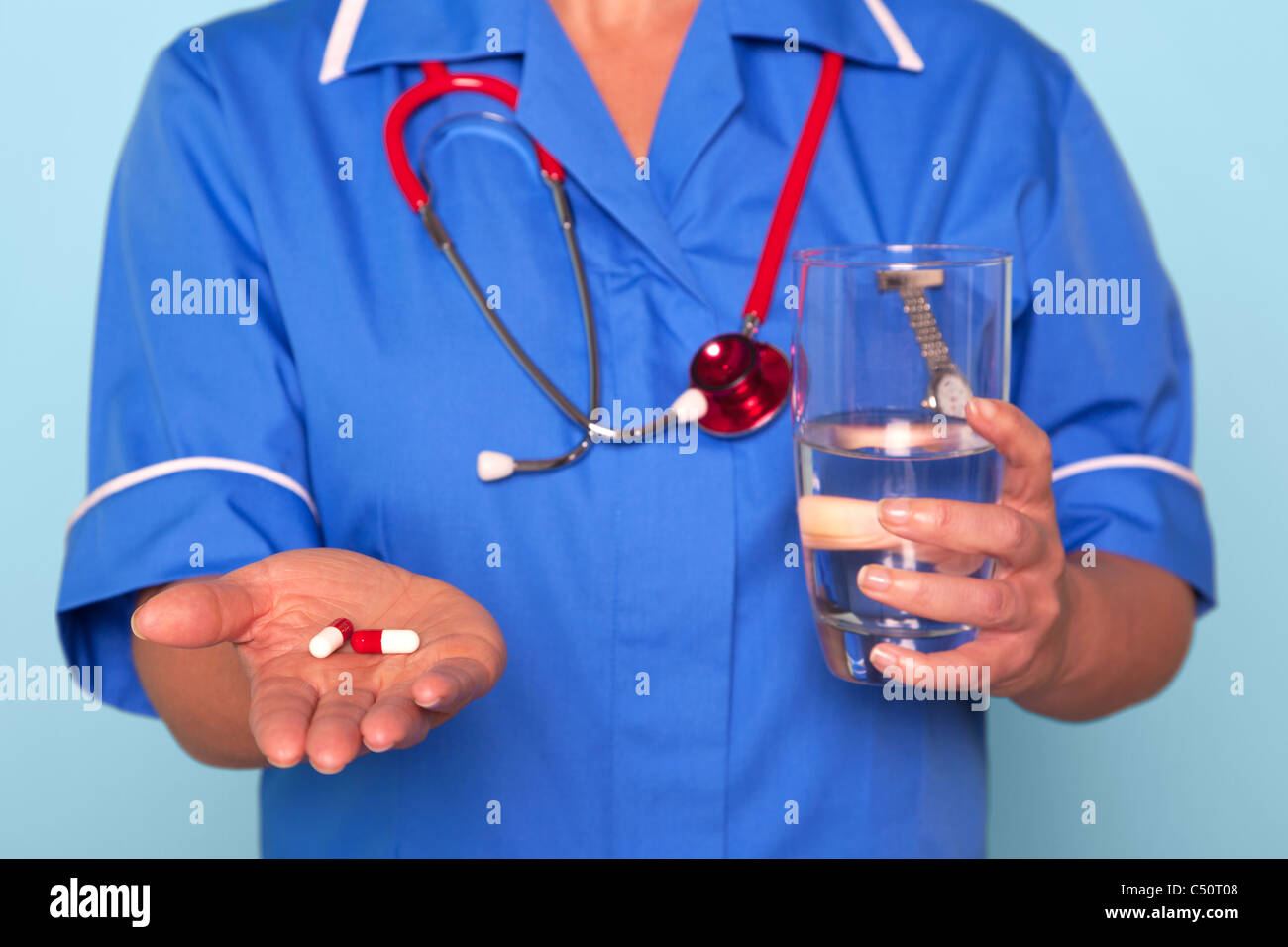 Foto von einer Krankenschwester in Uniform halten einige Pillen und ein Glas Wasser Stockfoto