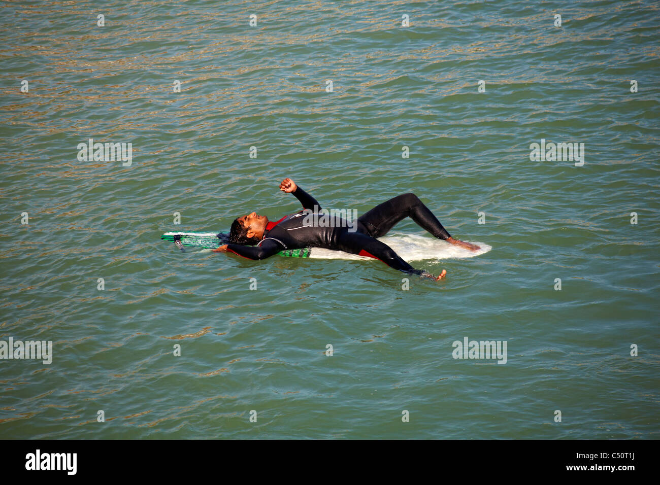 Surfer im Neoprenanzug liegend auf seinem Surfbrett, genießen die Sonne in Bournemouth im September Stockfoto