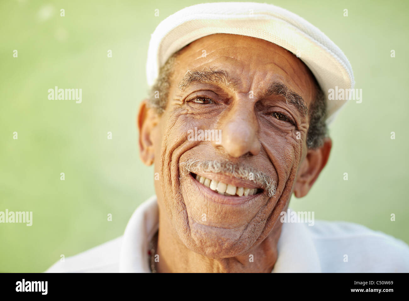 Porträt von senior hispanic Mann mit weißen Hut Blick in die Kamera gegen grüne Wand und lächelnd. Horizontale Form, Textfreiraum Stockfoto