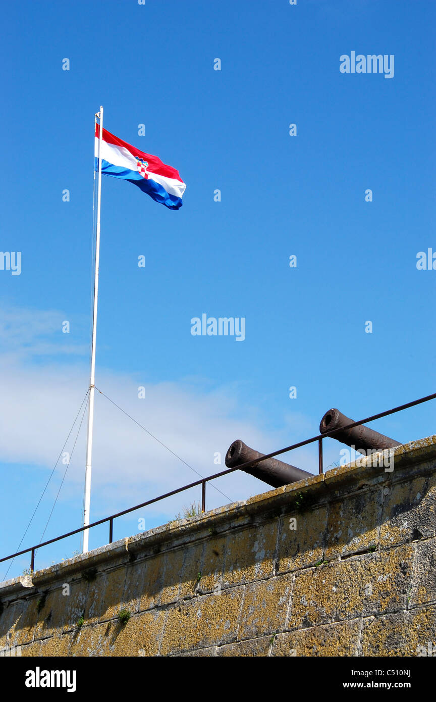 Kroatische Fahne flattert im Wind gegen blauen Himmel, oben eine Wand mit Kanonen hervorstehenden. Nationalismus-Konzept veranschaulicht. Stockfoto