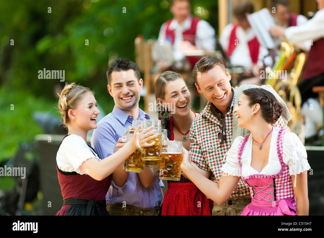 Im Biergarten in Bayern, Deutschland - Freunde in Tracht, Dirndl und Lederhosen und Dirndl stand vor band Stockfoto