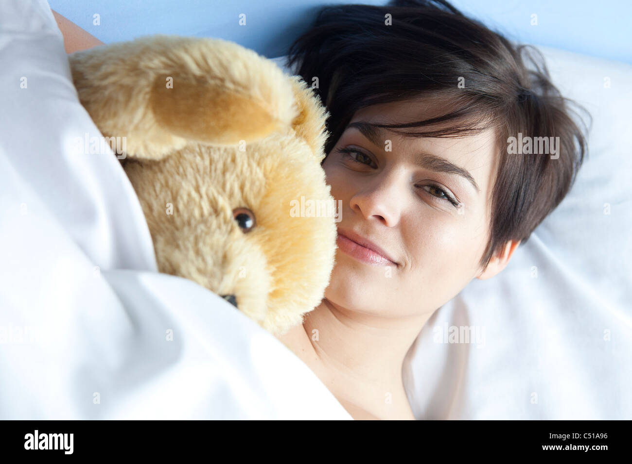Porträt der jungen Frau liegt im Bett mit Kuscheltier Stockfoto