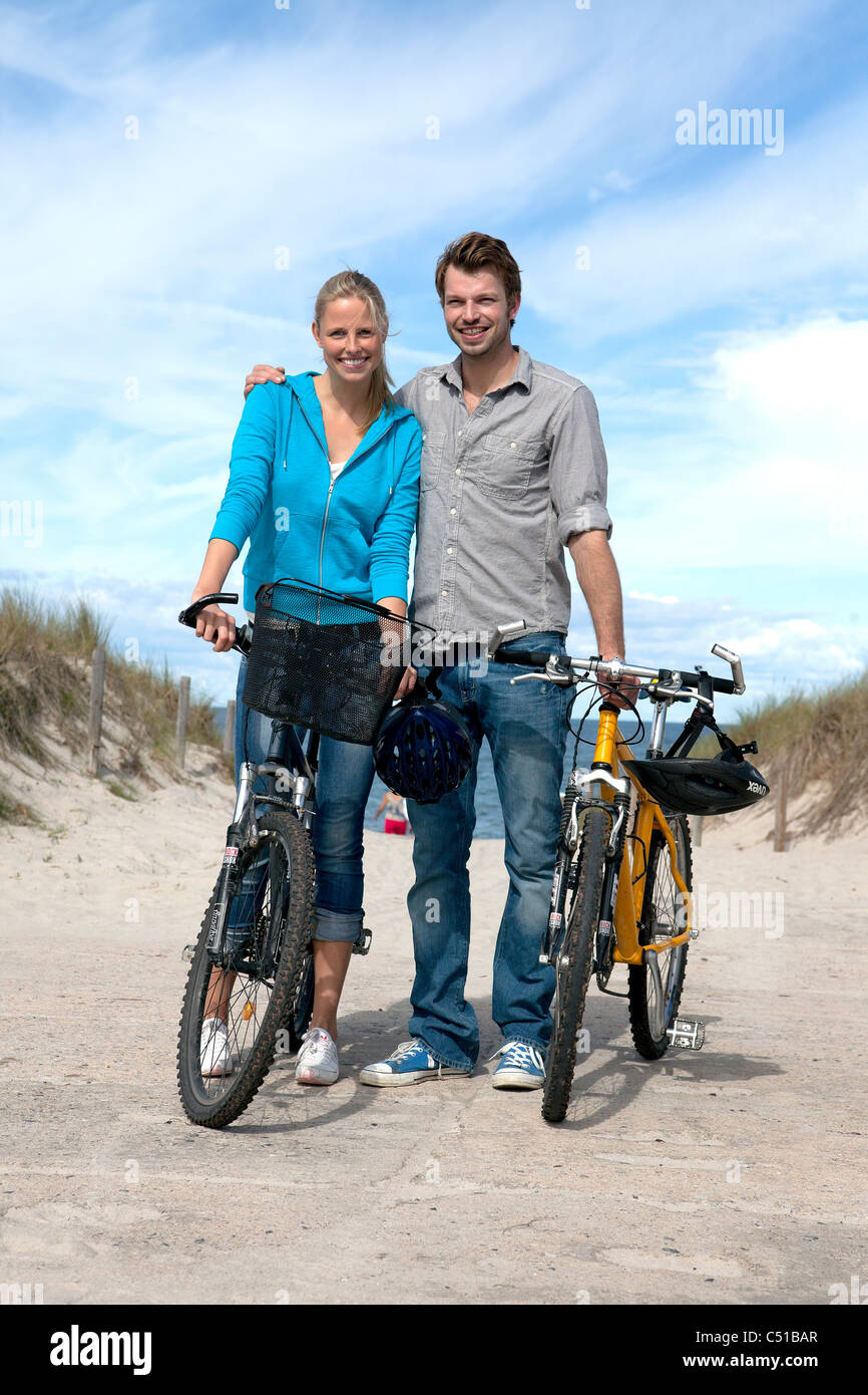 Porträt des jungen Paares mit Fahrrädern am Strand Stockfoto