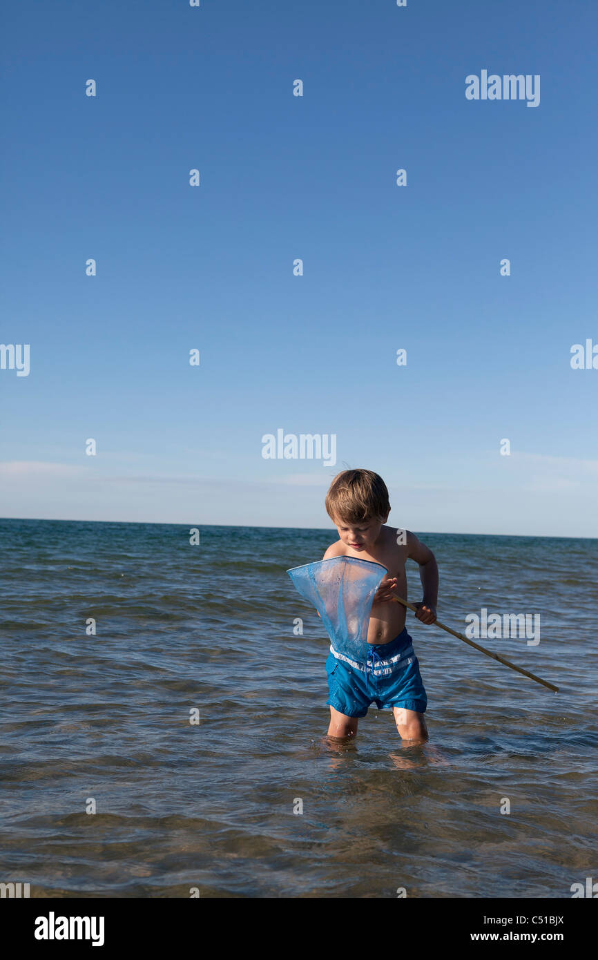 kleiner Junge stehend im Wasser Blick auf Fang in Löffel net Stockfoto