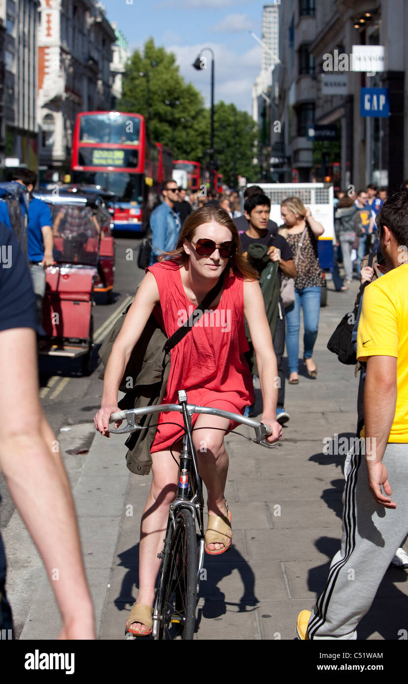 Frau-Radfahrer, die mit dem Fahrrad auf dem Bürgersteig unter Fußgänger, Oxford Street, London, England, UK Stockfoto
