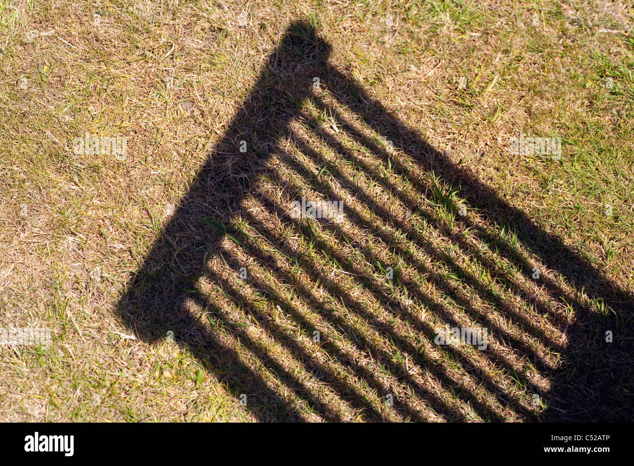 Shadow Cast über eine trockene und braune Garten Rasen durch eine hölzerne Gartenstuhl in der Sommersonne. Stockfoto