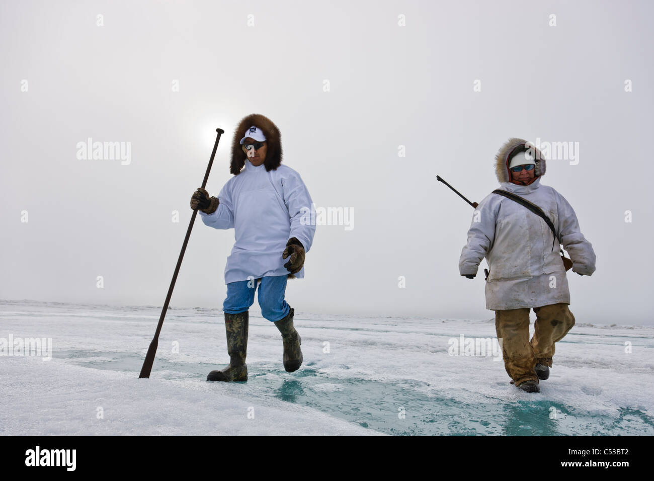 Inupiaq Eskimo Jäger tragen ein Gewehr und Gehstock bei einem Spaziergang über das Ufer Eis entlang der Tschuktschensee, Barrow, Alaska Stockfoto