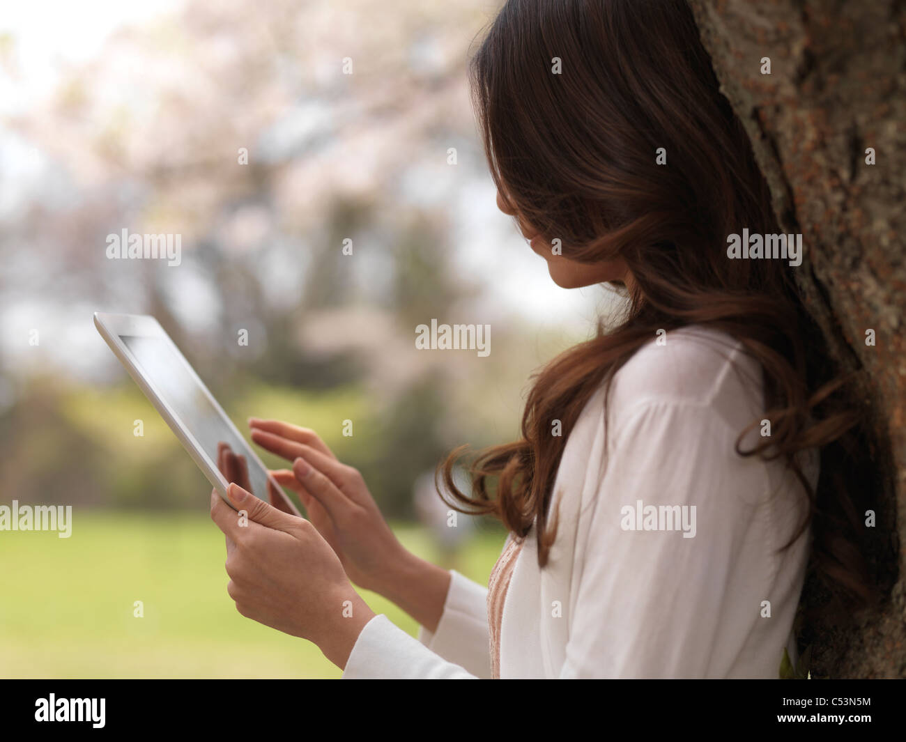 Lizenz erhältlich unter MaximImages.com - Young Woman mit iPad Tablet-Computer in einem Park unter einem Kirschbaum Stockfoto