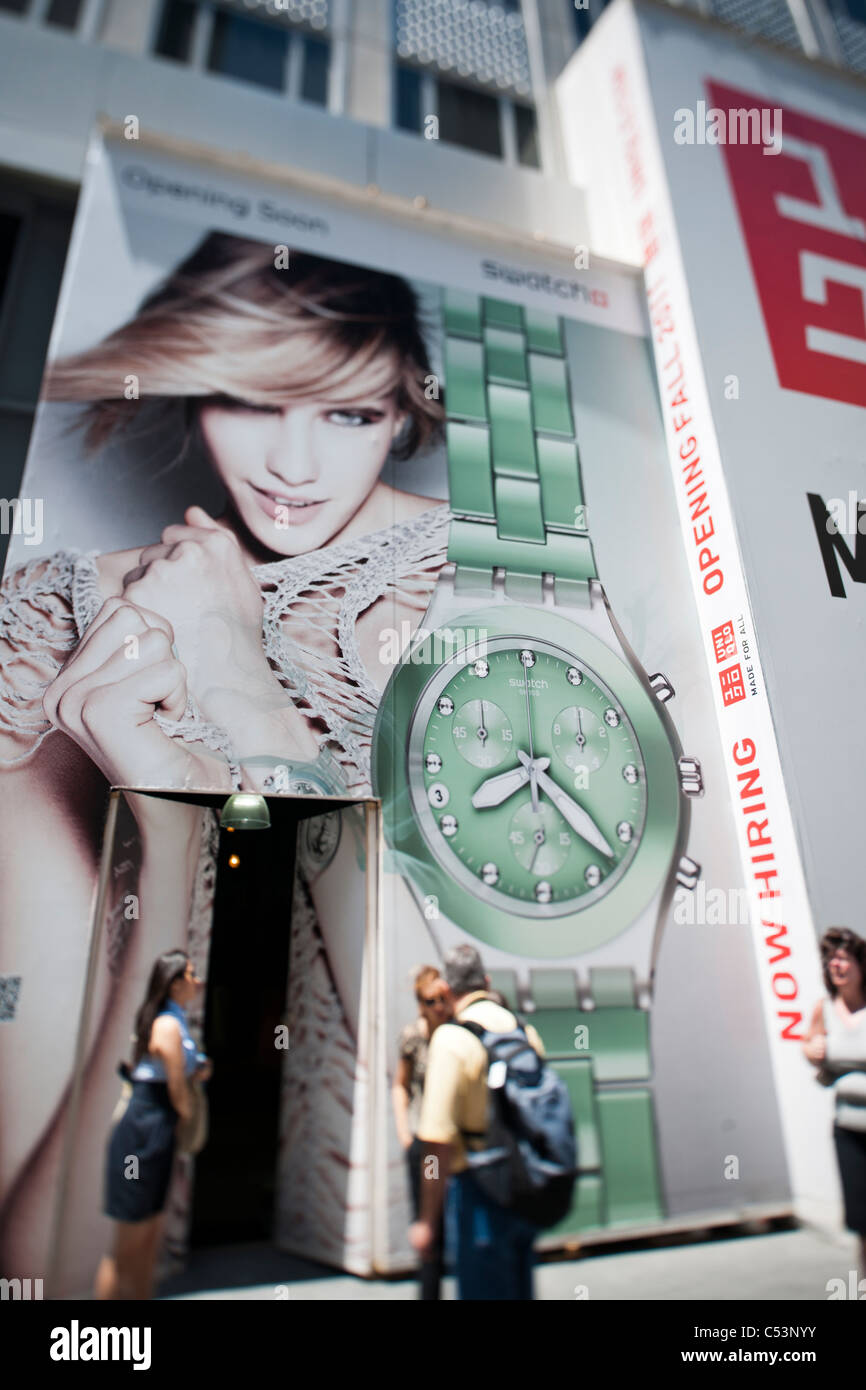 Ein Plakat auf einer Konstruktion, die Schuppen auf der Fifth Avenue in New York kündigt die eminente Ankunft einen Swatch store Stockfoto