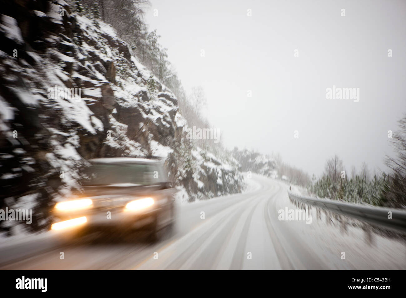 Verschneite Bergstraße mit einem Auto beschleunigen durch, während der Himmel mit einer weißen Schneedecke bedeckt ist Stockfoto