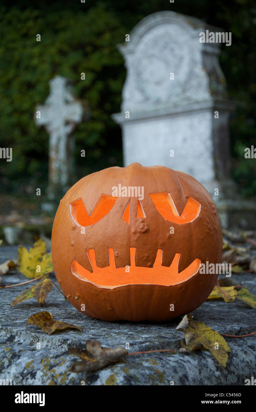 Die gespenstische grinsenden Gesicht einer Halloween Jack o'Lantern aus einem Kürbis geschnitzt, glühende bei Kerzenschein, in einem alten Friedhof. England, Vereinigtes Königreich. Stockfoto