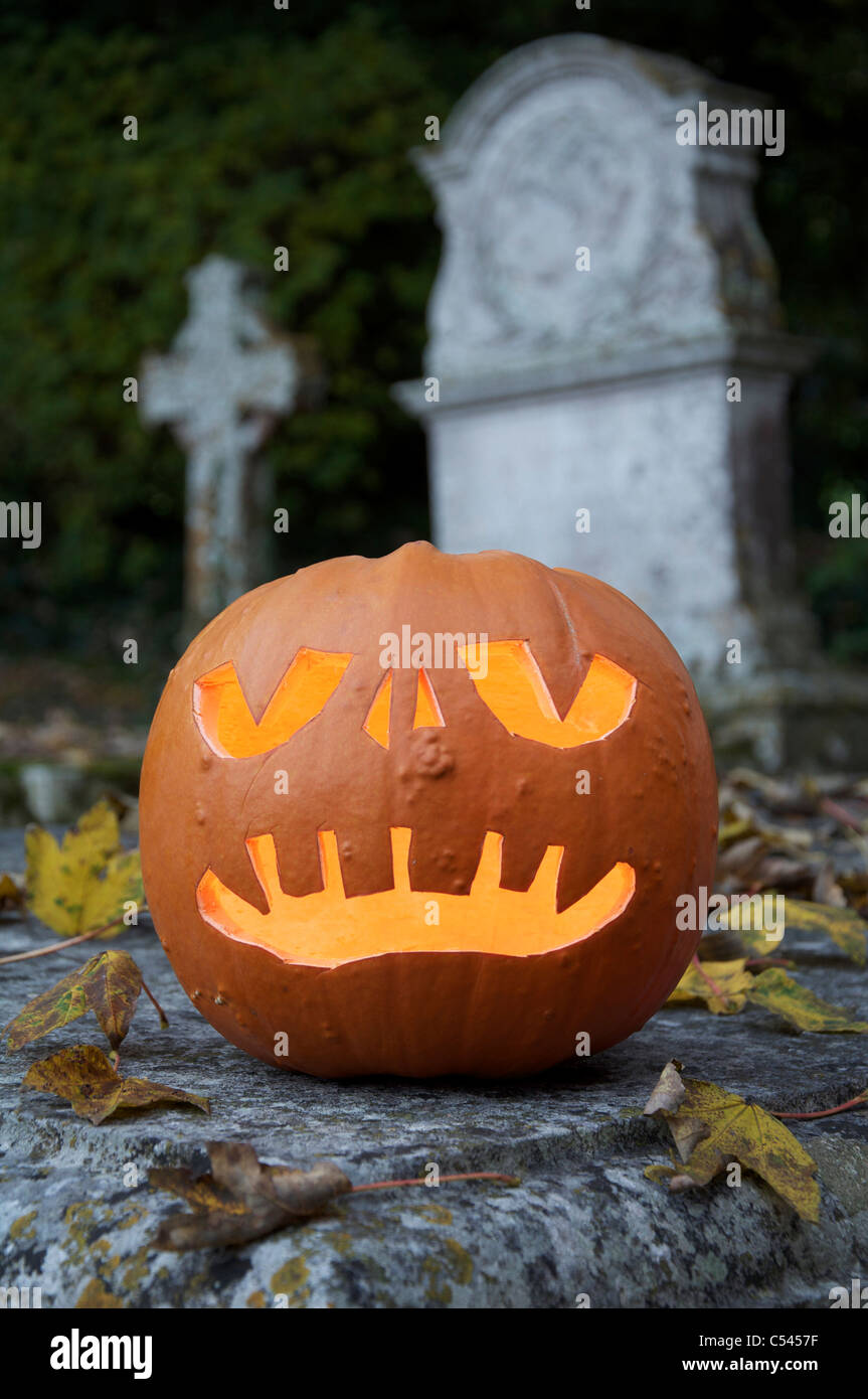 Die gespenstische grinsenden Gesicht einer Halloween Jack o'Lantern aus einem Kürbis geschnitzt, glühende bei Kerzenschein, in einem alten Friedhof. England, Vereinigtes Königreich. Stockfoto