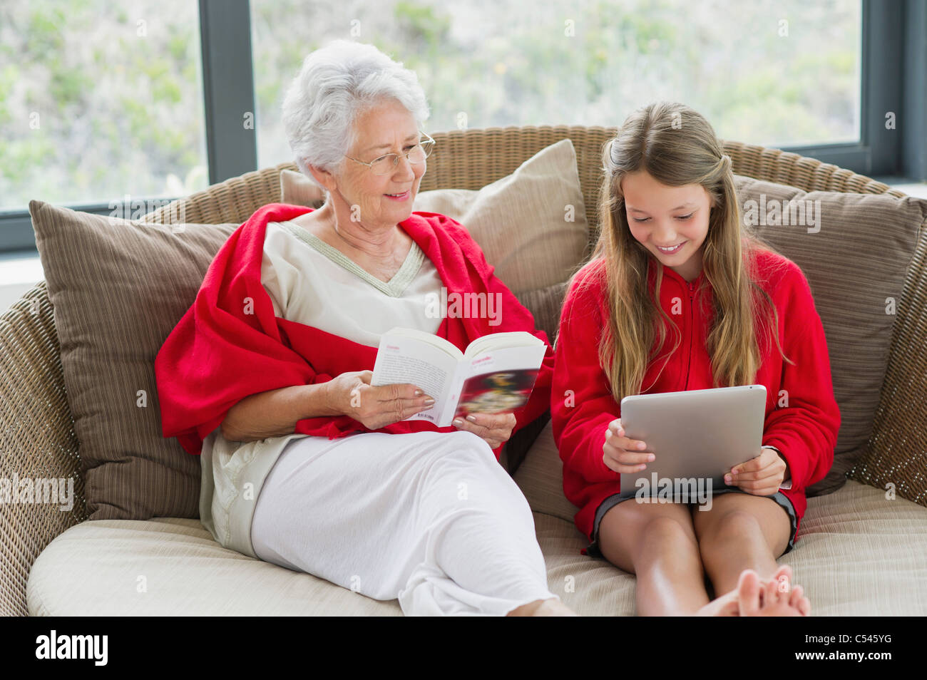 Ältere Frau mit ihrer Enkelin mit einem digitalen Tablet eine Zeitschrift liest Stockfoto