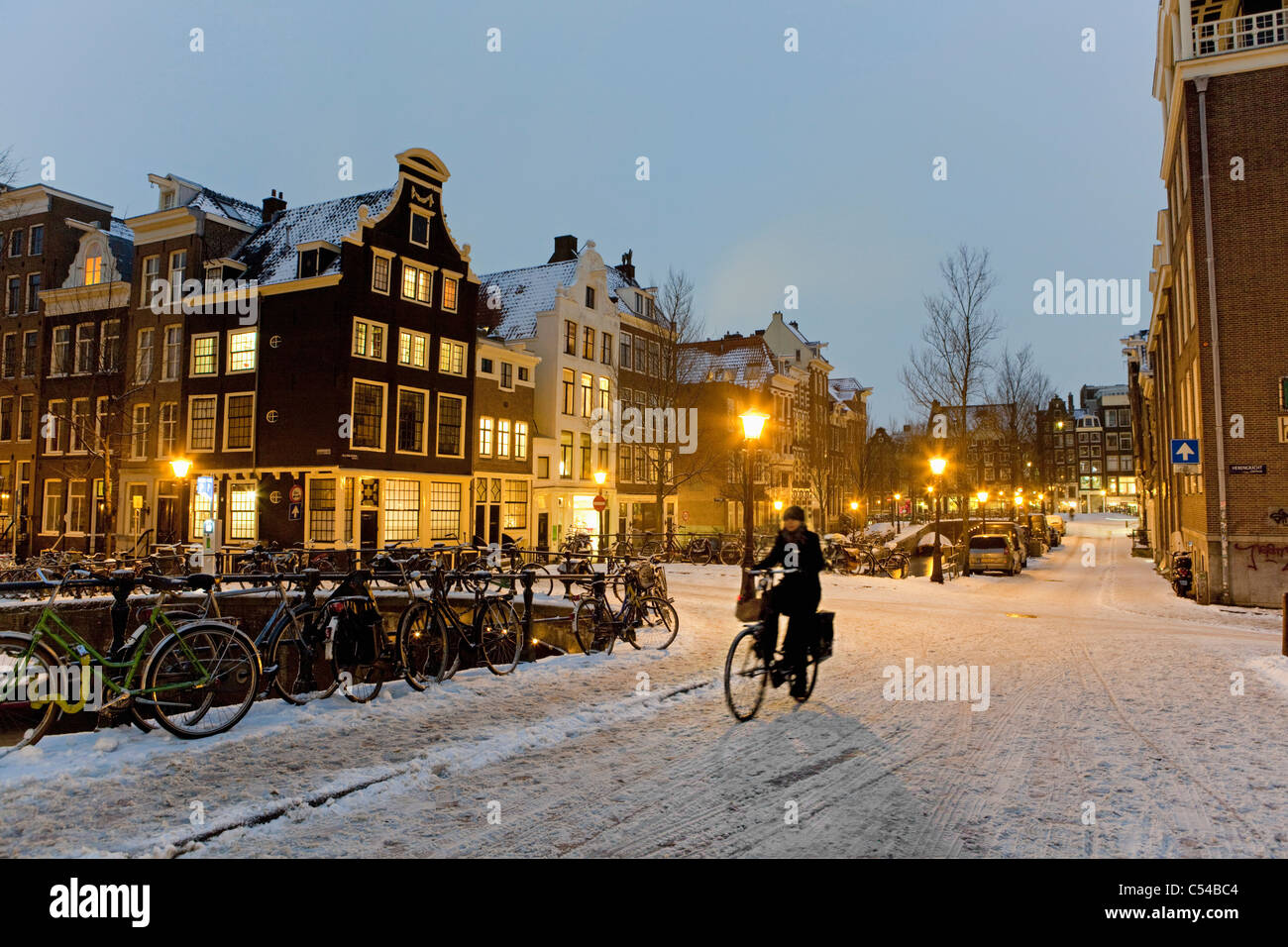 Niederlande, Amsterdam, Winter, Schnee. Radfahrer auf Kanalbrücke in der Abenddämmerung. Stockfoto