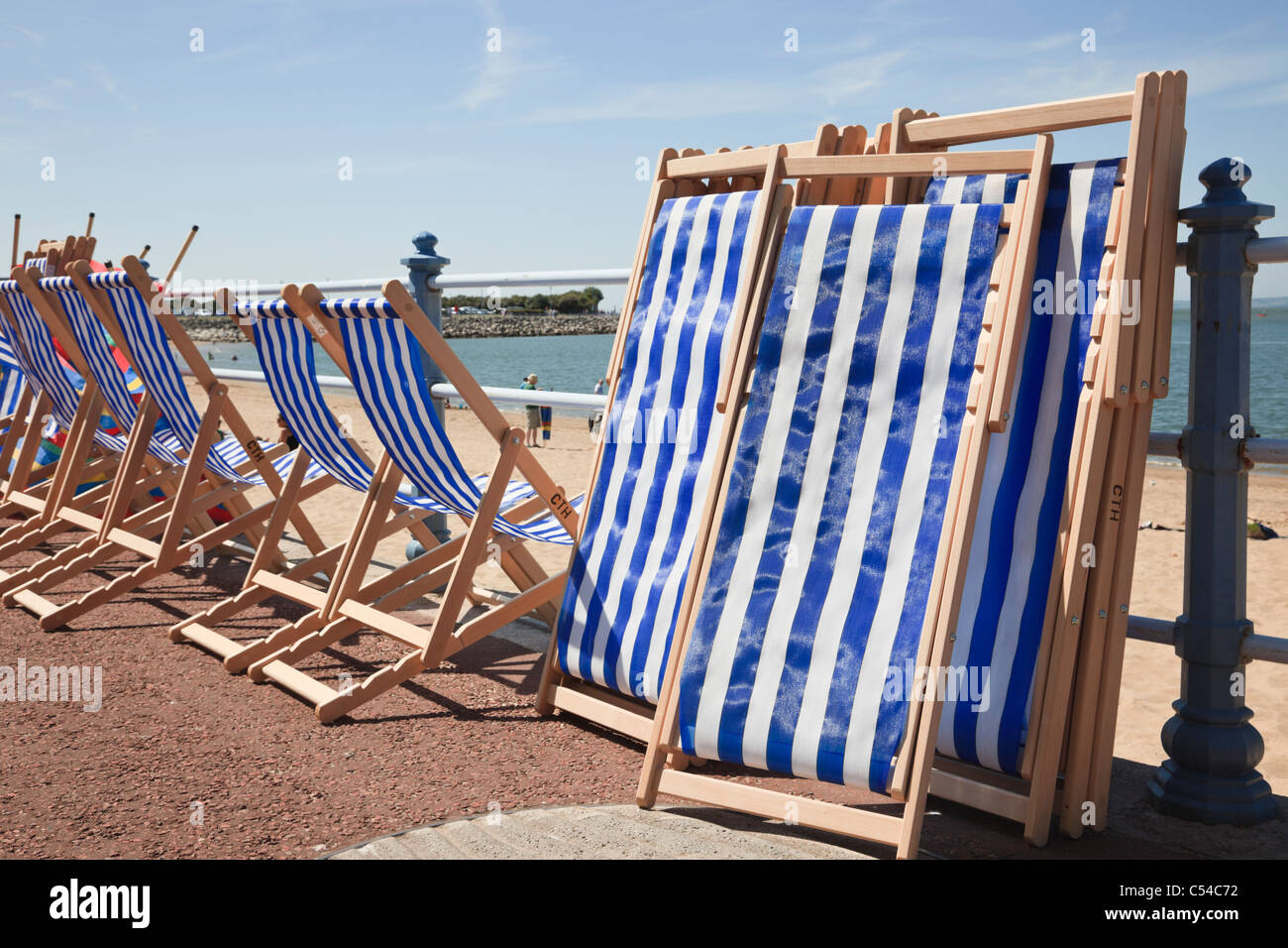 Blau-weiß gestreifte Liegestühle können im Hochsommer an einer Strandpromenade am Strand gemietet werden. Morecambe, Lancashire, England, Großbritannien. Stockfoto