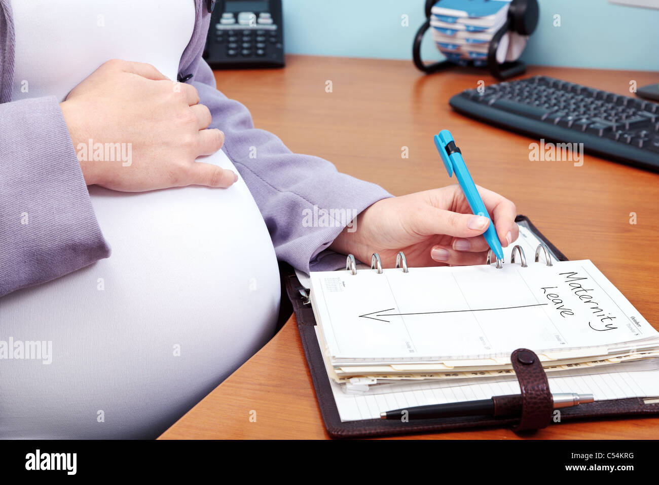 Foto von einer schwangeren Frau in einem Büro die Worte Mutterschaftsurlaub in ihr Tagebuch zu schreiben. Stockfoto