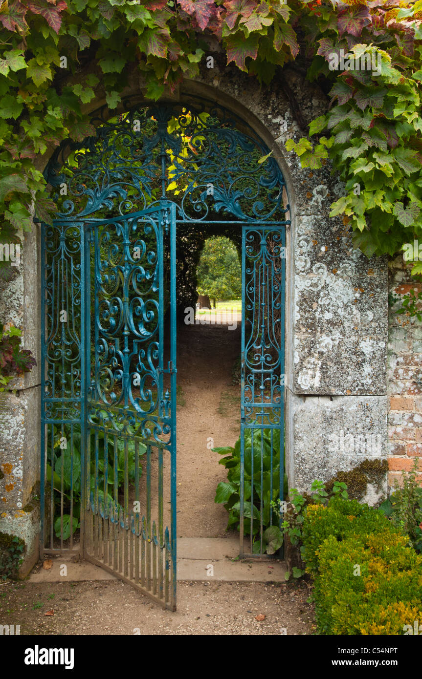 Kunstvolles schmiedeeisernes Tor in einem Cotswold-Steinbogen, eingerahmt von Weinblättern. Blick aus dem ummauerten Garten im Rousham House, Oxfordshire, England Stockfoto