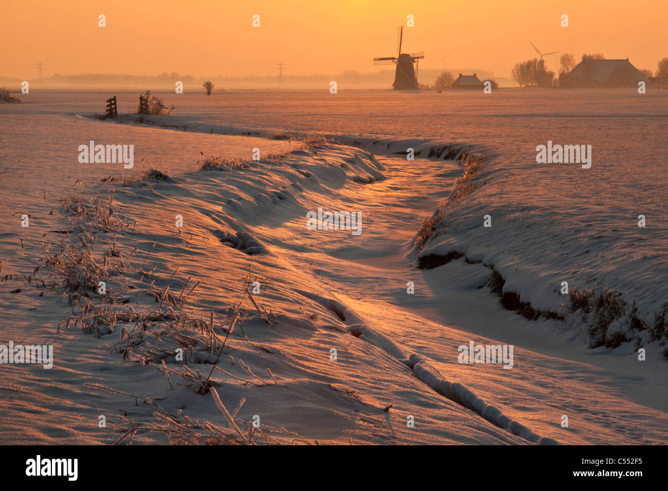 Niederlande, Lollum, Windmühle und gefrorenen Bach im Schnee bei Sonnenuntergang. Stockfoto