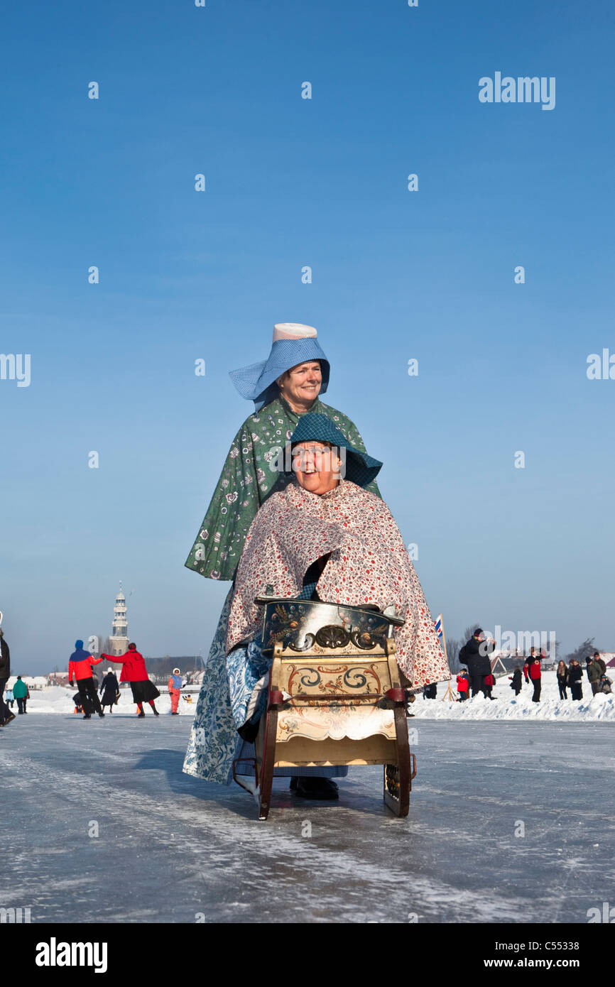 Niederlande, Hindeloopen, niederländische Hauptstadt des Eislaufs Kultur. Frauen gekleidet in traditioneller Tracht mit Schlitten auf Eis. Stockfoto