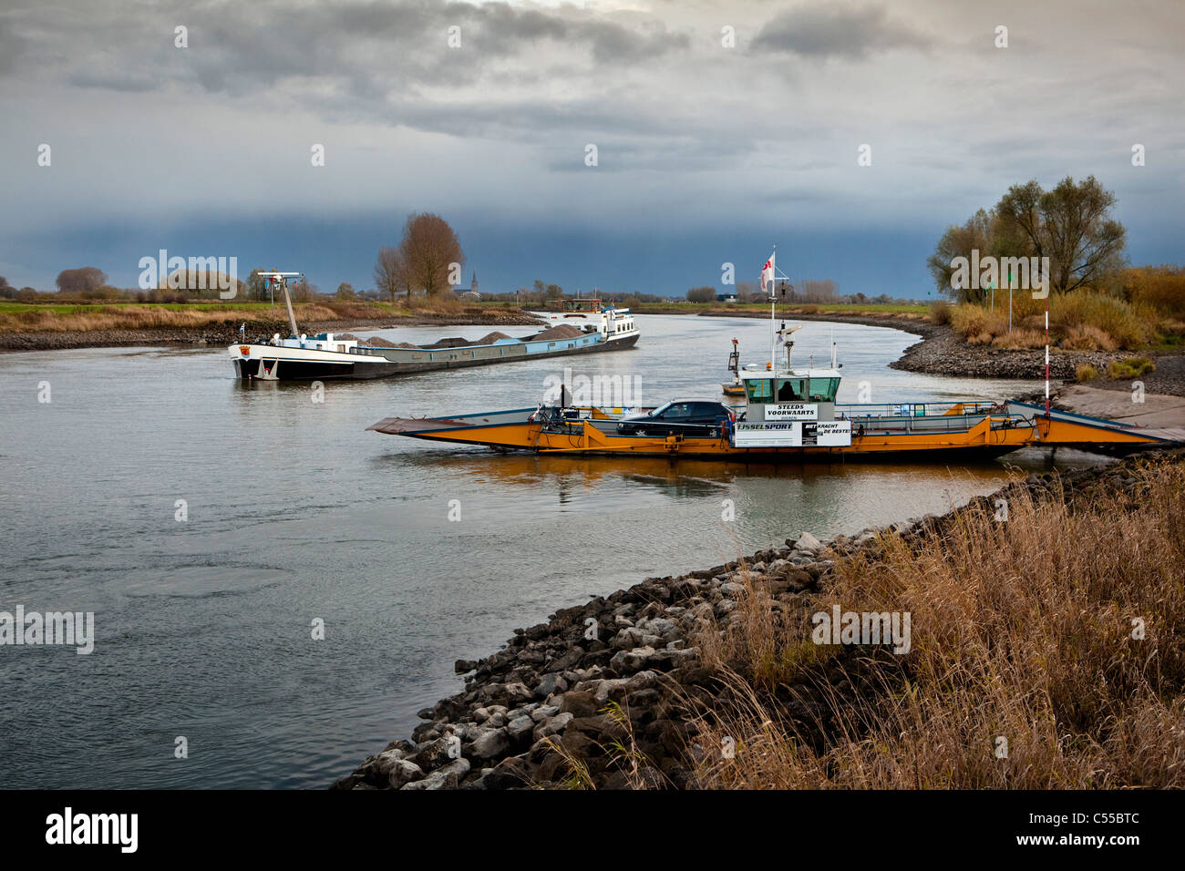 Der Niederlanden, in der Nähe von Doesburg, Cargo Schiff und Auto Fähre am Fluss IJssel. Stockfoto