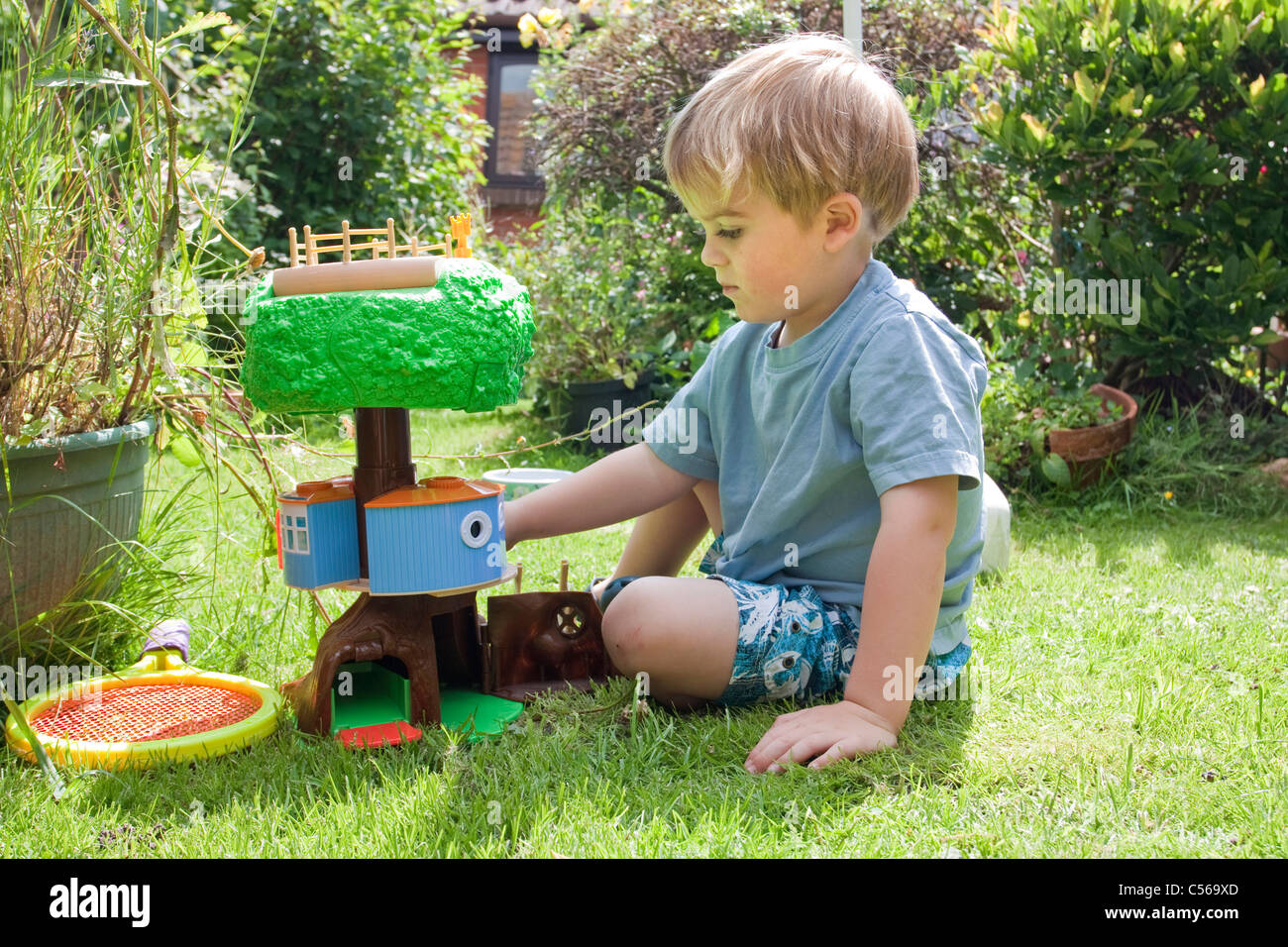 Kleinkind niedlichen blonden Jungen spielen draußen im Garten mit einem Kunststoff Baum = Haus Spielzeug Stockfoto