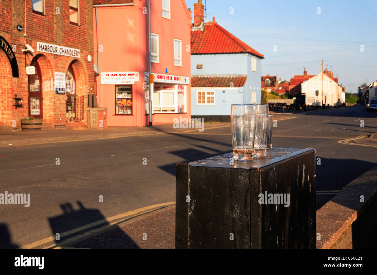 Drei leere Biergläser links am Straßenrand auf dem Kai am Brunnen neben Meer, Norfolk, England, Vereinigtes Königreich. Stockfoto