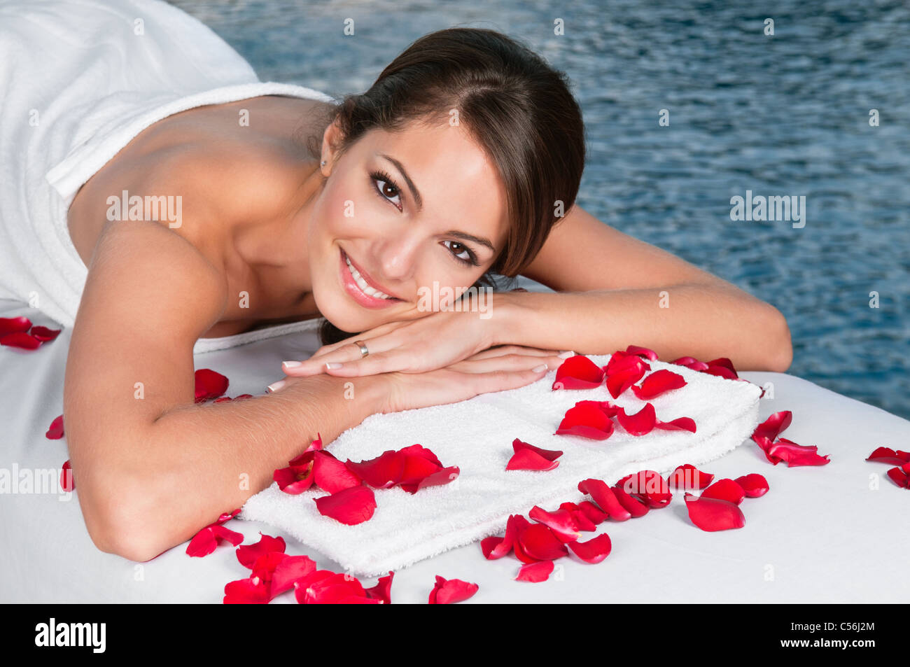 Porträt der schönen jungen weiblichen auf Massagebett liegend mit Rosenblüten im Vordergrund Stockfoto
