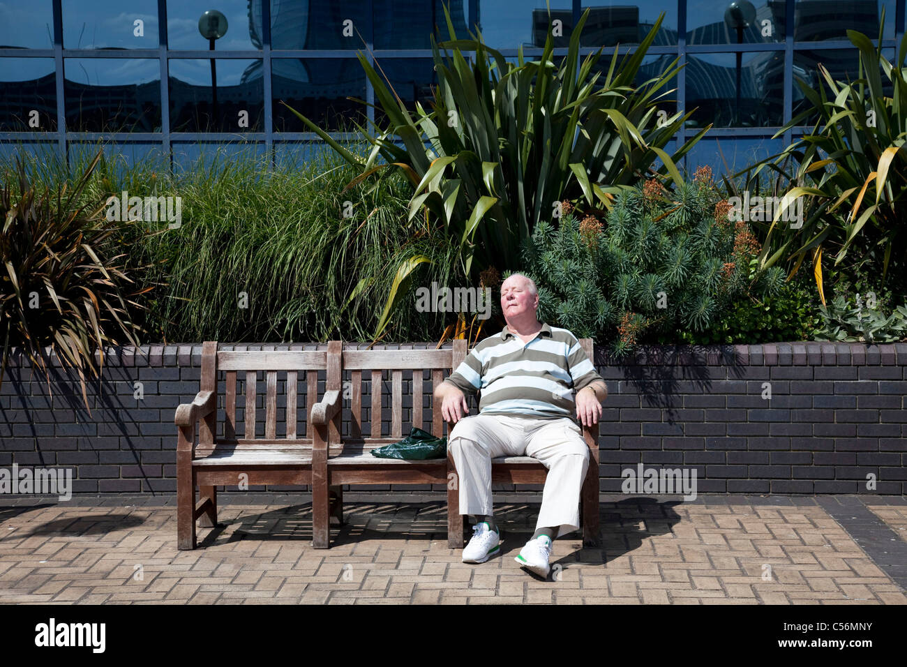 Mann schläft auf einer Bank in der Sonne. London. Stockfoto