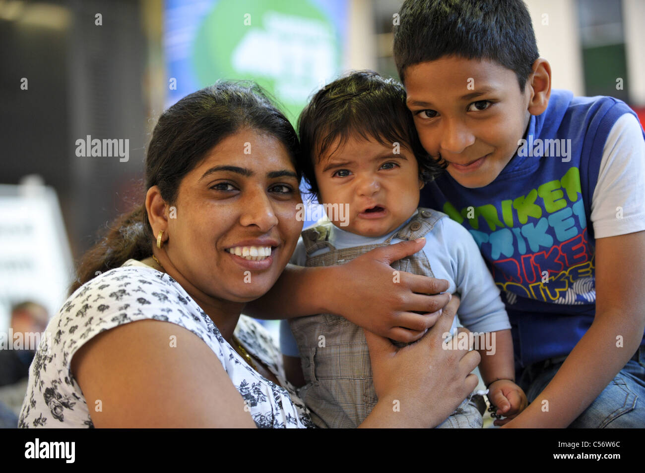Bristish Sikh Mutter lächelnd mit ihren zwei Söhnen, einem einem weinenden baby andererseits ein frecher kleiner Junge Stockfoto