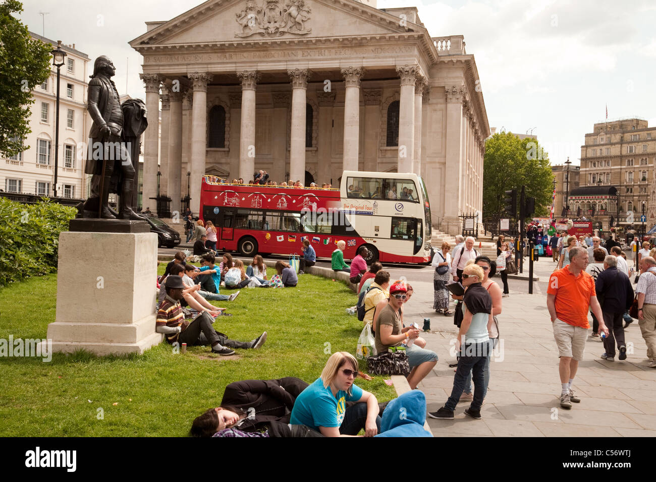 Menschen sitzen auf dem Rasen in Trafalgar Square außerhalb der National Gallery, St Martin in the Fields im Hintergrund, London Stockfoto