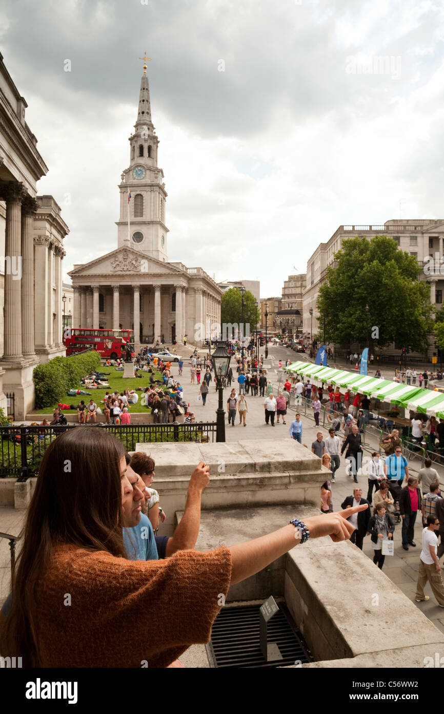 Menschen sitzen auf dem Rasen in Trafalgar Square außerhalb der National Gallery, St Martin in the Fields im Hintergrund, London Stockfoto