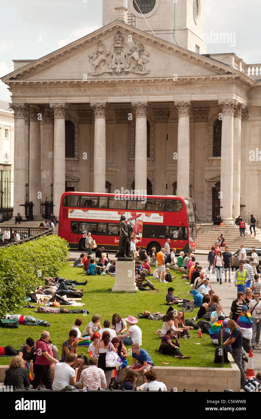 Menschen sitzen auf dem Rasen in Trafalgar Square außerhalb der National Gallery, St Martin in the Fields im Hintergrund, London Stockfoto