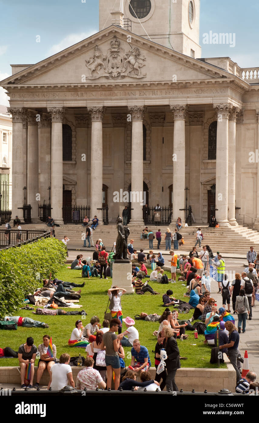 Menschen sitzen auf dem Rasen in Trafalgar Square außerhalb der National Gallery, St Martin in the Fields im Hintergrund, London Stockfoto