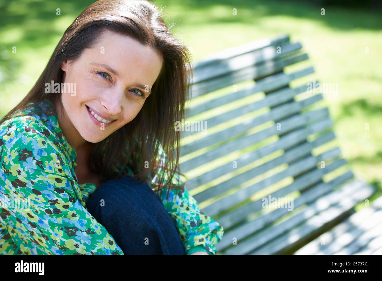 Lächelnde Frau sitzt auf der Parkbank Stockfoto