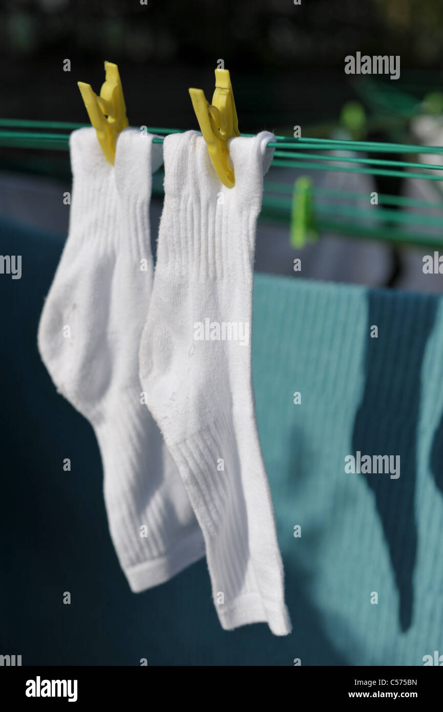 zwei weiße Sportsocken und blaues Handtuch gekoppelt auf einer Wäscheleine in der Frühlingssonne Stockfoto