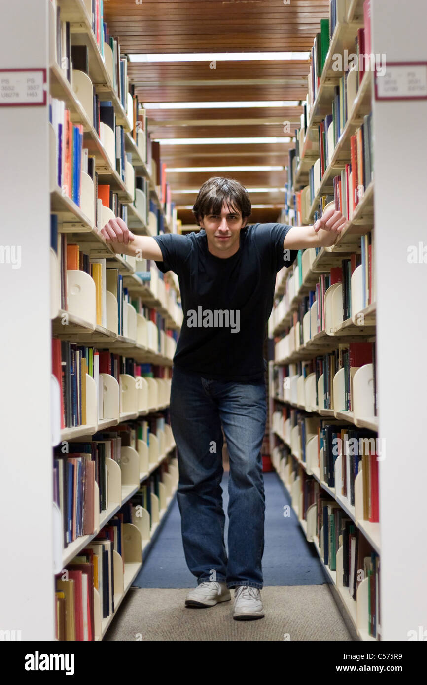 Ein junger Mann in den Gängen der Bibliothek Buchregale stehen. Stockfoto
