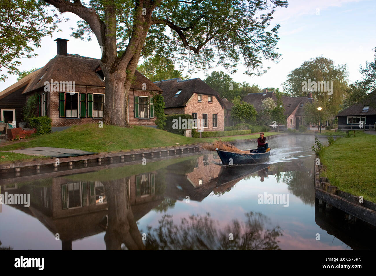 Die Niederlande, Dwarsgracht, in der Nähe von Giethoorn. Dorf mit fast nur Wasserstraßen. Häuser in der Morgendämmerung. Landwirt Transport Reed für roofconstruction. Stockfoto