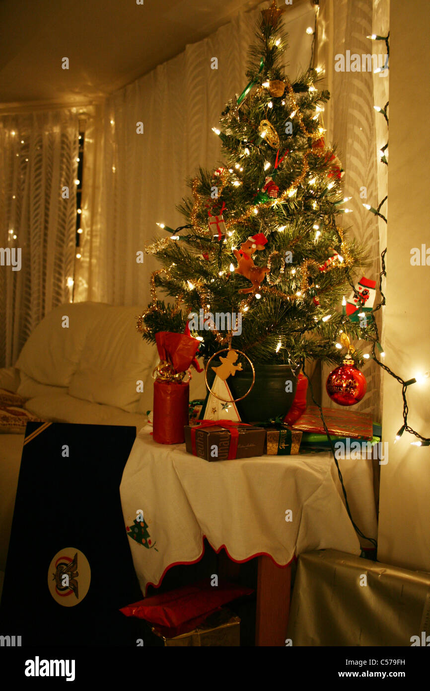 Kleiner Weihnachtsbaum auf Tisch in glühenden Wohnzimmer mit Lichtern und  weiße Ledercouch und verpackte Geschenke rund um Baum Stockfotografie -  Alamy